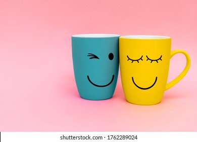 Valentine's day concept. Two happy cups yellow and turquoise colors on pink background.