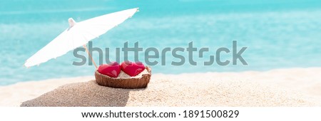 Valentines day concept. Two hearts - symbol of love couple on sand paradise tropical beach under parasol. Blue sea and sky in background. Love, togetherness, marriage. Traveling together. Wide banner
