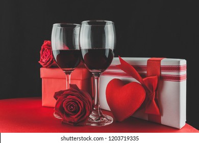 Valentine's Day Concept, White Wrapped Gift Box With Red Ribbon, Rose Flower Petals, Red Wine Glass, With Red Candle, On Dark Stone Background