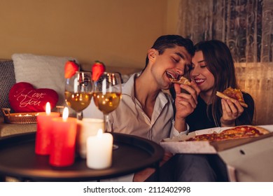 Valentines Day couple in love eating pizza drinking wine with strawberries having romantic dinner celebrating at home at night - Powered by Shutterstock