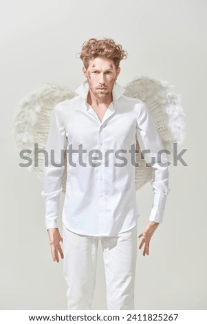 Valentine's Day. Courageous handsome male Cupid angel in white clothes and with white wings. White background. God of love Cupid. 