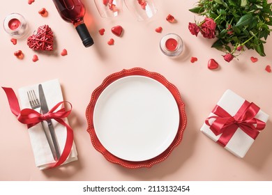 Valentines day dinner with gift, red wine, roses and hearts on pink background. Top view. Copy space. Valentine's greeting card.