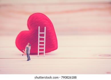 Valentine's day / eternal love or special occasion concept : Love couple miniature figurine hug / embrace each other to express affection near a red pillow heart with a white ladder on wood floor.