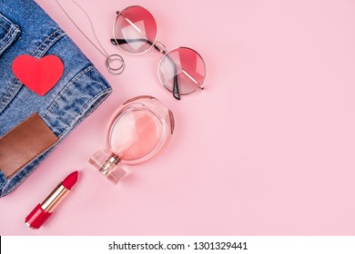 Valentine's day fashion   beauty flatlay and blue mom jeans  bottle perfumes  red lipstick  gradient round sunglasses  minimalistic necklace   paper heart pink background 