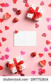 Valentine's Day flat lay composition. Top view blank paper card, gifts, hearts on pink table. Valentines day greeting card mockup.