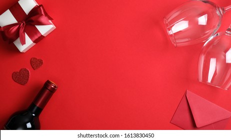 Valentines Day Frame. Flat Lay White Gift Box With Red Ribbon Bow, Bottle Of Wine Champagne, Two Glasses And Envelope On Red Background. Valentines Day Celebration, Romantic Dinner Couple Concept