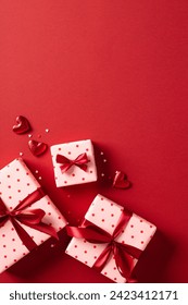 Valentines day gifts with red ribbon bow, hearts, confetti on red vertical background.