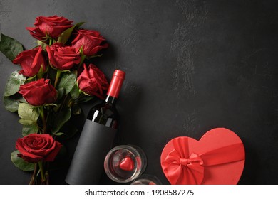 Valentine's day greeting card with red roses and wine and hearts gift on black background with copy space.
