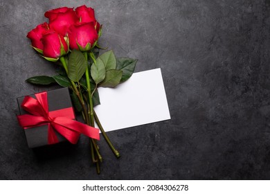 Valentines Day Greeting Card With Red Rose Flowers Bouquet And Gift Box On Stone Table. Top View Flat Lay With Space For Your Greetings