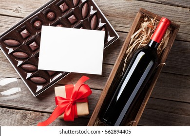 Valentines Day Greeting Card. Red Wine, Gift Box And Chocolate Box On Wooden Table. Top View With Space For Your Greetings 