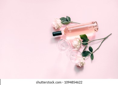 Valentines day greeting card.  White roses, wine and glasses for wine on a soft light pink on wood table. Flat lay, top view, copy space