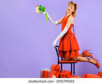 Valentines Day. Happy girl with gift and bouquet of tulips. Smiling Woman in red dress with flowers and gift