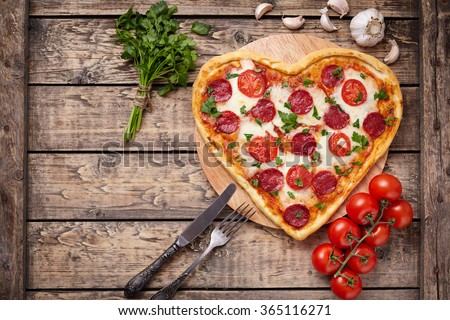 Valentines day heart shaped pizza with pepperoni, cherry tomatoes, mozzarella and parsley on vintage wooden table background. Symbol of love.
