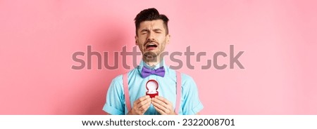 Valentines day. Heartbroken guy crying and holding engagement ring, sobbing from break-up, standing over pink background.