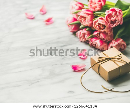 Valentines day holiday background. Bouquet of pink tulips and gift box with ribbon over white marble table background. Pink tulips and gift box with copy space. Lovers or Womens day greeting card