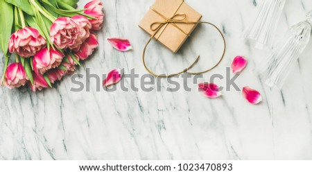Valentines day holiday background. Flat-lay of pink tulips bouquet, champaign glasses and gift box with ribbon over white marble table, top view, copy space. Lovers or Womens day greeting card