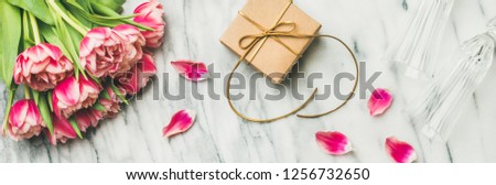 Valentines day holiday background. Flat-lay of pink tulips bouquet, champaign glasses and gift box with ribbon over white marble table, top view. Lovers or Womens day greeting card