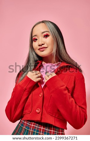 Valentines day, jolly asian young woman with heart eye makeup posing in red jacket on pink