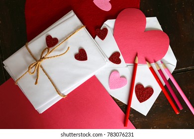 Valentine's Day Letter Art Supplies Including: Red And Pink Colored Pencils, Construction Paper, Heart Shaped Stickers, And A Stack Of Envelopes With A Twine String Bow Are Sitting On A Table.