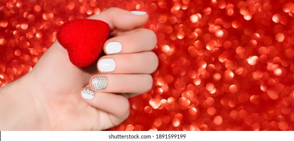 Valentine's Day Nail Design. White Nail Design With Glitter Nail Art. Female Hand Hold Red Heart On Red Bokeh Backgound.