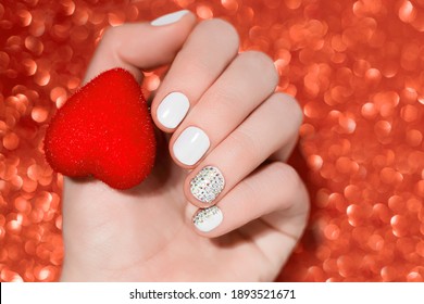 Valentine's Day Nail Design. White Nail Design With Glitter Nail Art. Female Hand Hold Red Heart On Red Bokeh Backgound.