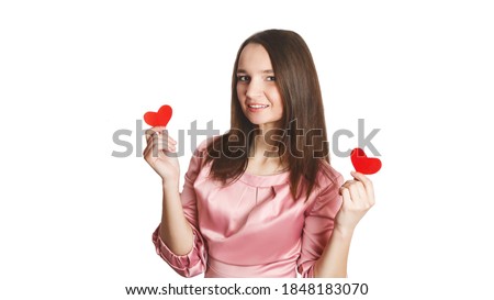 Valentine's Day. Pretty young beautiful caucasian women in pink dress holding two small paper heart in hands ith beaming toothy smile on white background. Love concept. isolated