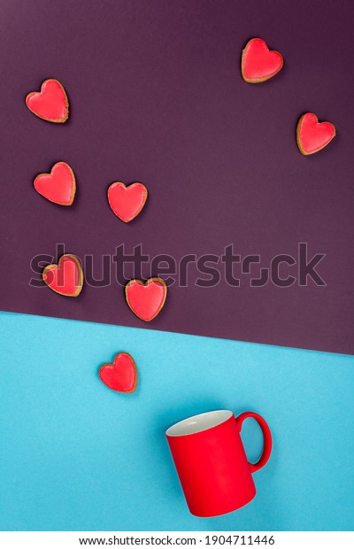 Valentine\'s Day, red heart shaped cookies on\
blue and purple paper background flying out from a  tilted  red\
mug, flat lay. Love and Valentine\'s Day\
concept.