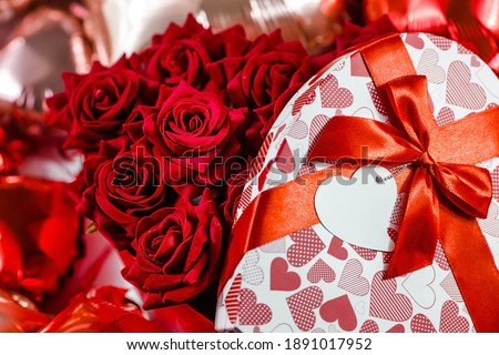 Valentine's day. Red roses in a white box in the form of a heart on the background of foil balls. A gift for women on a holiday. The concept of delivering flowers. floristry and flower shops. 