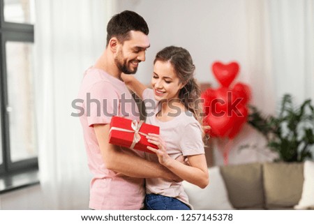 valentines day, relationships and people concept - happy couple with gift box hugging at home