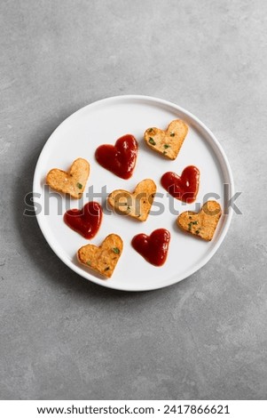 Valentine's Day roasted potato hearts and red sauce hearts on a white plate on concrete background. Romantic food ideas for Valentine's Day. Top view, copy space