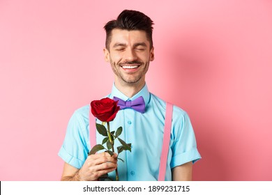 Valentines day and romance concept. Romantic man with red rose going on date with lover, standing in fancy bow-tie on pink background