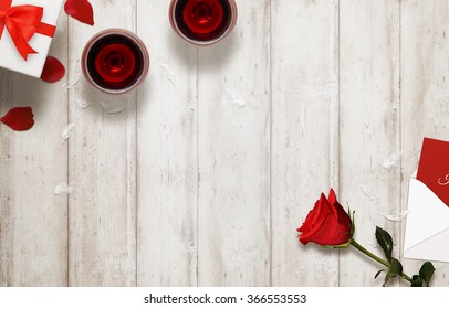 Valentines Day Romantic Background With Glasses Of Wine, Gift, Envelope, Rose On Wooden Table.