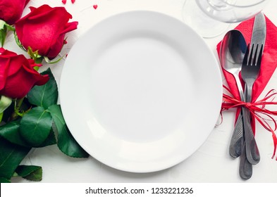 Valentine's Day Romantic Tabble Setting With Red Roses, Plates, Cutlery On White Background. Empty Plate. Mockup Design Layout For Your Text. Love Valentines Concept. Copy Space. Top View. Flat Lay.