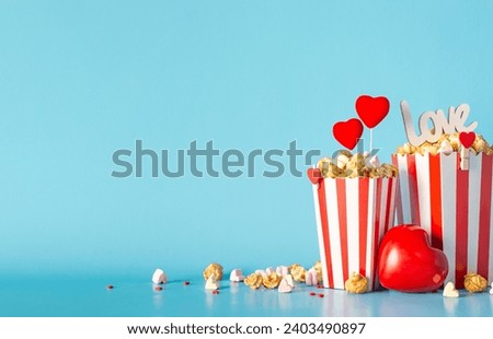 Valentine's Day at romantic theater. Side view reveals table adorned with striped containers loaded with caramel popcorn, heart-themed accents, love-inscribed sign, and more on light blue background