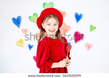 valentine's day, a small smiling child girl in a red beret happy holds or licks a large lollipop in the form of a heart and rejoices against the background of colorful hearts.