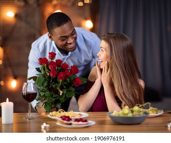 Valentine's Day Surprise. Elegant African American Man Giving Roses Bouquet To His Beautiful Girlfriend During Romantic Dinner In Restaurant, Loving Multiracial Couple Dining Together, Free Space - Powered by Shutterstock