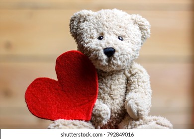 Valentine's Day. Teddy bear with red heart on wooden background.