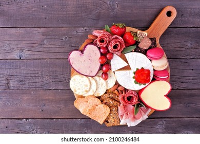 Valentine's Day theme charcuterie board with a selection of cheeses, appetizers and sweets. Overhead view on a dark wood background. - Powered by Shutterstock