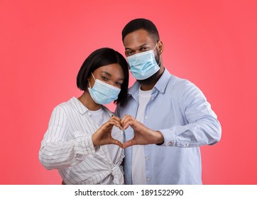 Valentine's Day At Times Of Coronavirus. Romantic African American Couple Making Heart With Hands, Wearing Protective Masks On Pink Background. Black Sweethearts Demonstrating Love Gesture