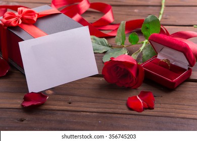 Valentine's Day: White empty paper card, red roses, gold ring and box gift with ribbons on rustic brown wooden background. - Powered by Shutterstock