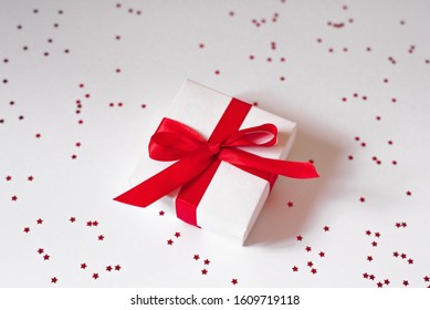 Valentine's day. White gift box with red satin ribbon on white background with confetti. Background of Valentine's day, Christmas or New Year. Creative greeting card - Shutterstock ID 1609719118