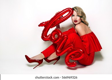 Valentine's Day. Word love letters from the inflatable. Girl holding a big word love.
Girl with retro hairstyle in red dress in red high heels sitting on the floor in studio on a white background.
