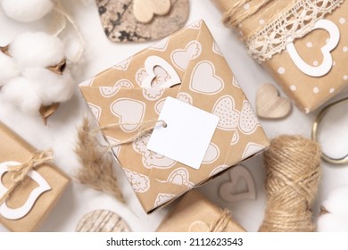 Valentines Kraft Paper Wrapped Present With Square Gift Tag And Hearts Close Up. Spring Scene With Blank Label. Rustic, Cottage Chic Or Bohemian Mockup, Copy Space