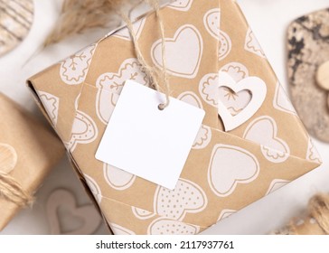 Valentines Kraft Paper Wrapped Present With Square Gift Tag And Hearts Close Up. Spring Scene With Blank Label. Rustic, Cottage Chic Or Bohemian Mockup, Copy Space