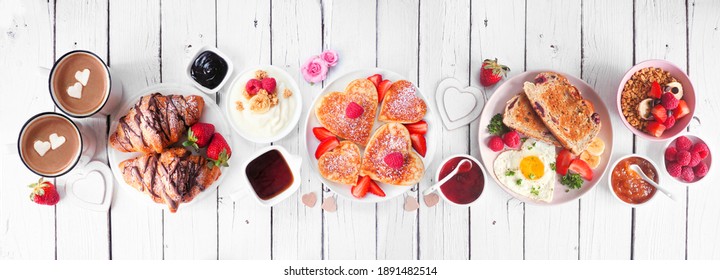 Valentines Or Mothers Day Breakfast Table Scene. Above View On A White Wood Banner Background. Heart Shaped Pancakes, Eggs And A Variety Of Love Themed Food.