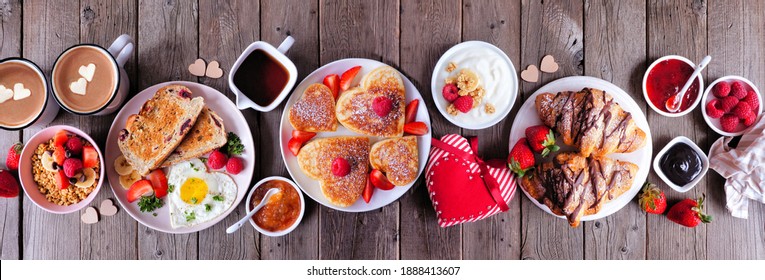 Valentines Or Mothers Day Brunch Table Scene. Overhead View On A Dark Wood Banner Background. Heart Shaped Pancakes, Eggs And A Variety Of Love Themed Food.