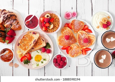 Valentines Or Mothers Day Brunch Table Scene. Top View On A White Wood Background. Heart Shaped Pancakes, Eggs And An Assortment Of Love Themed Food.