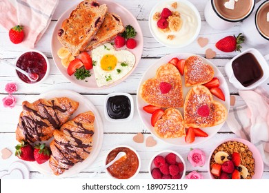 Valentines Or Mothers Day Brunch Table Scene. Overhead View On A White Wood Background. Heart Shaped Pancakes, Eggs And Assorted Love Themed Food.