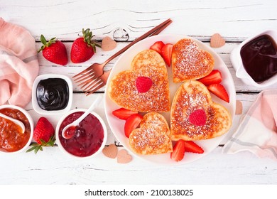Valentines or Mothers Day heart shaped pancakes. Overhead view on a white wood background.