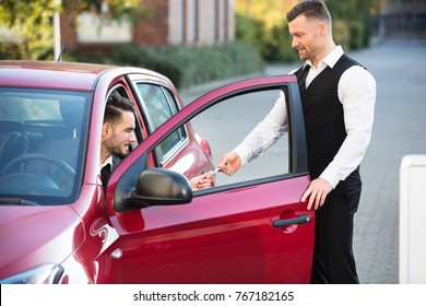 Valet Giving Receipt To Young Male Businessperson Sitting Inside Red Car